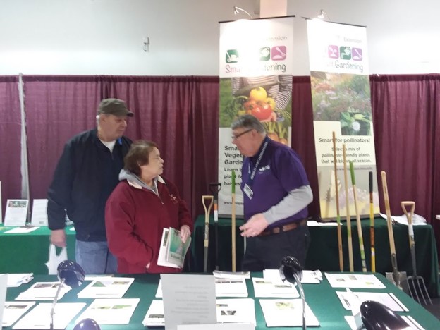 A volunteer talks to people at a garden conference.